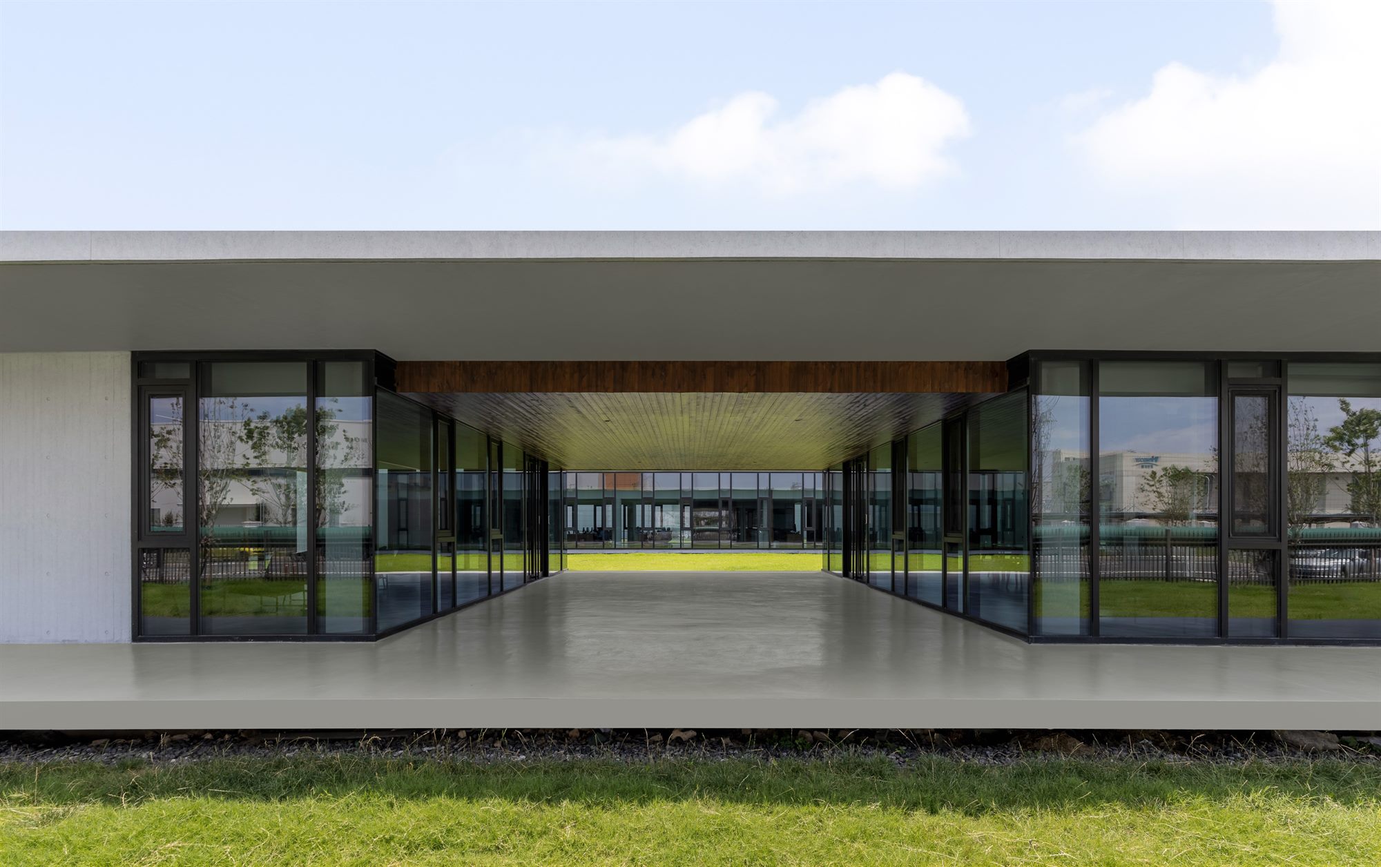 Glazed office pavilion with deep roof overhang above a lawn, Shihlien battery plant