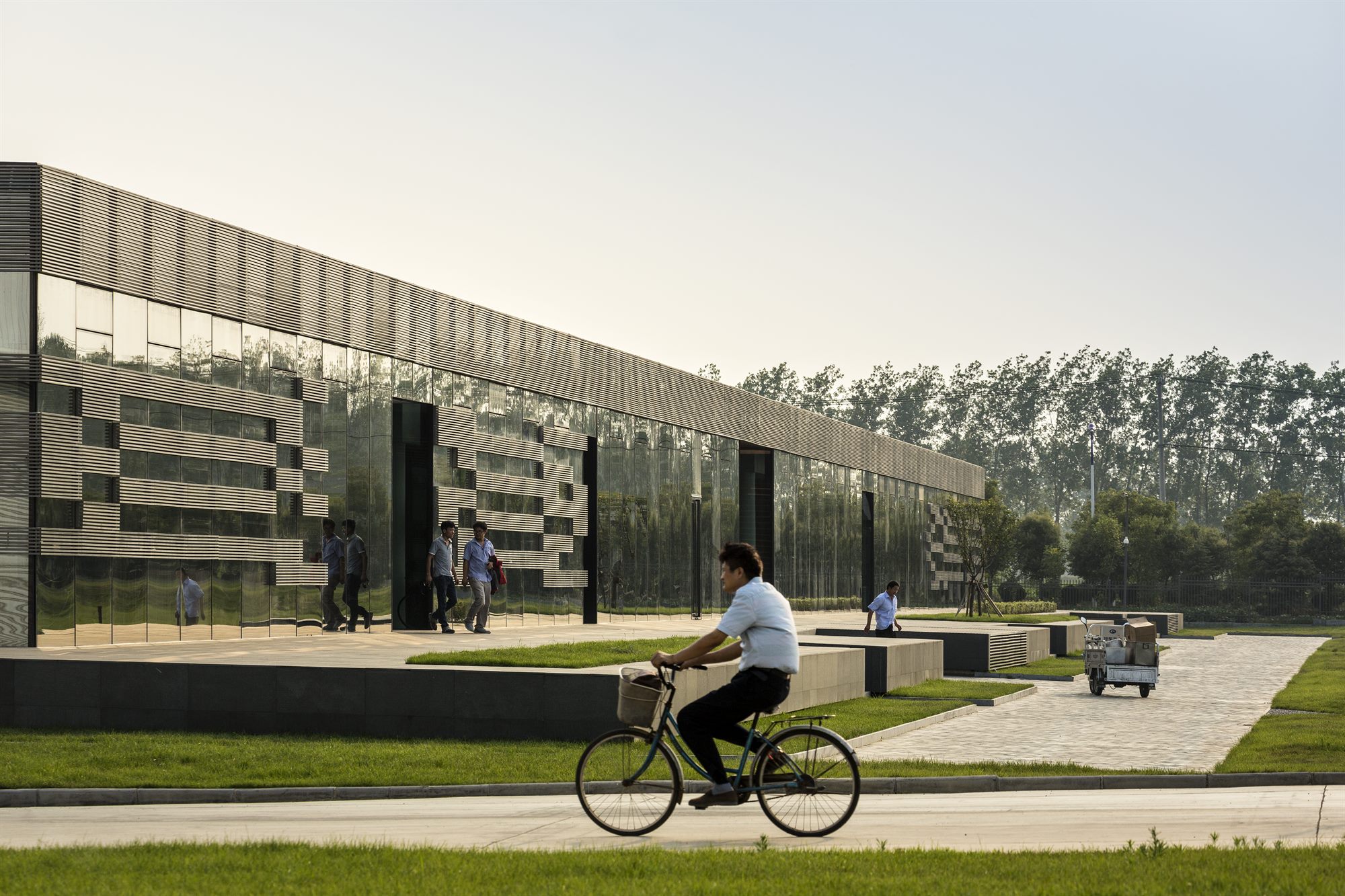 Cyclist passing the dark glass façade of the Donghai office building at dusk