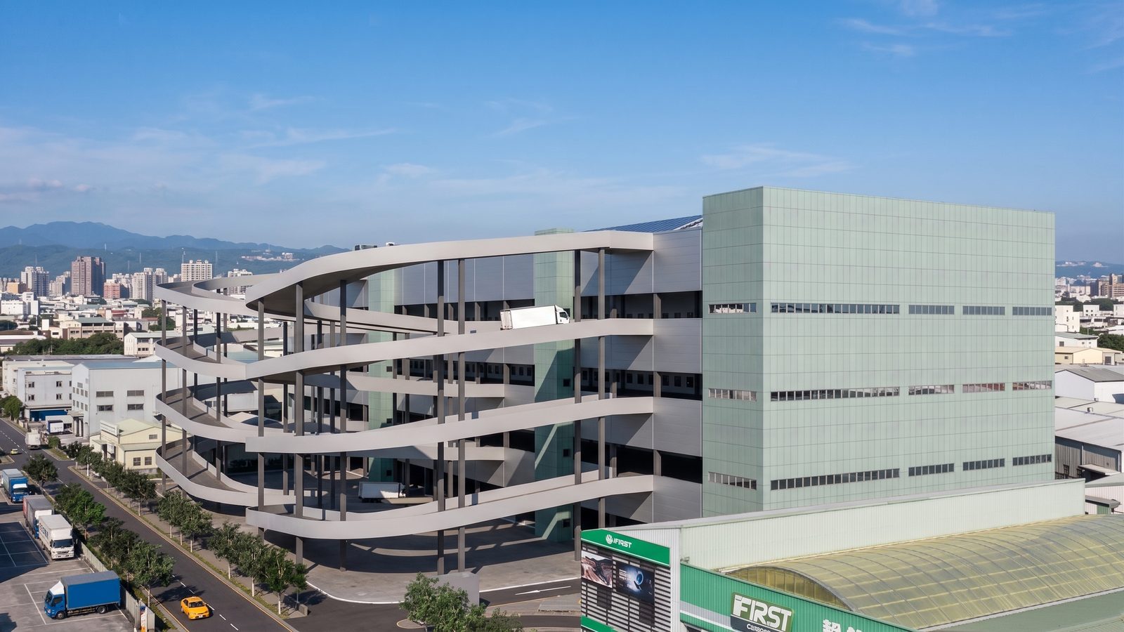 Rendering: corner view of the spiral truck ramps and green-grey cladding, logistics centre