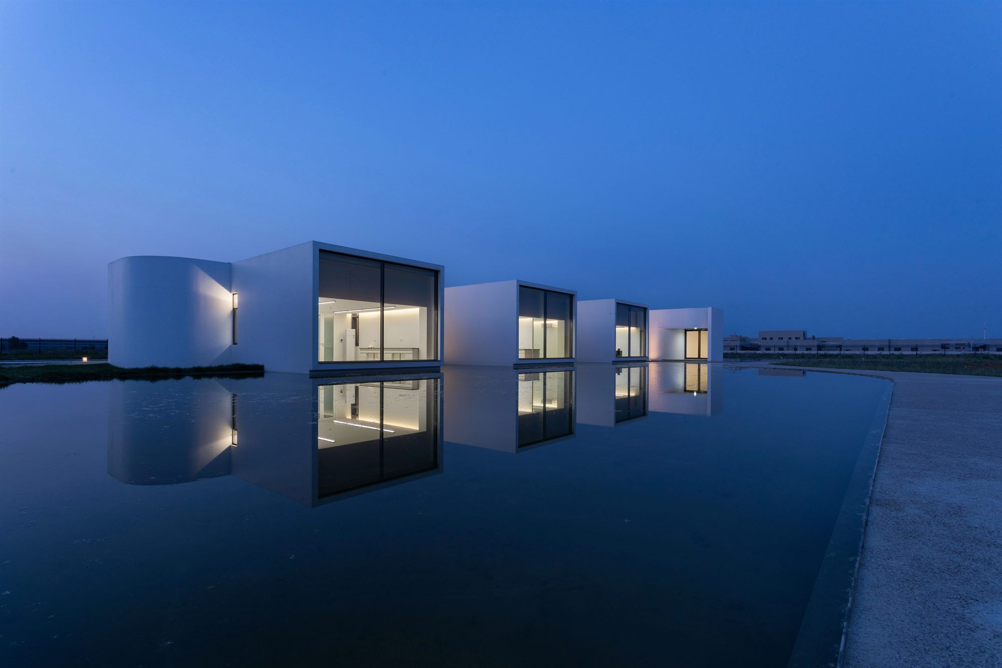 Salt laboratory at dusk, white volumes and lit windows reflected in water