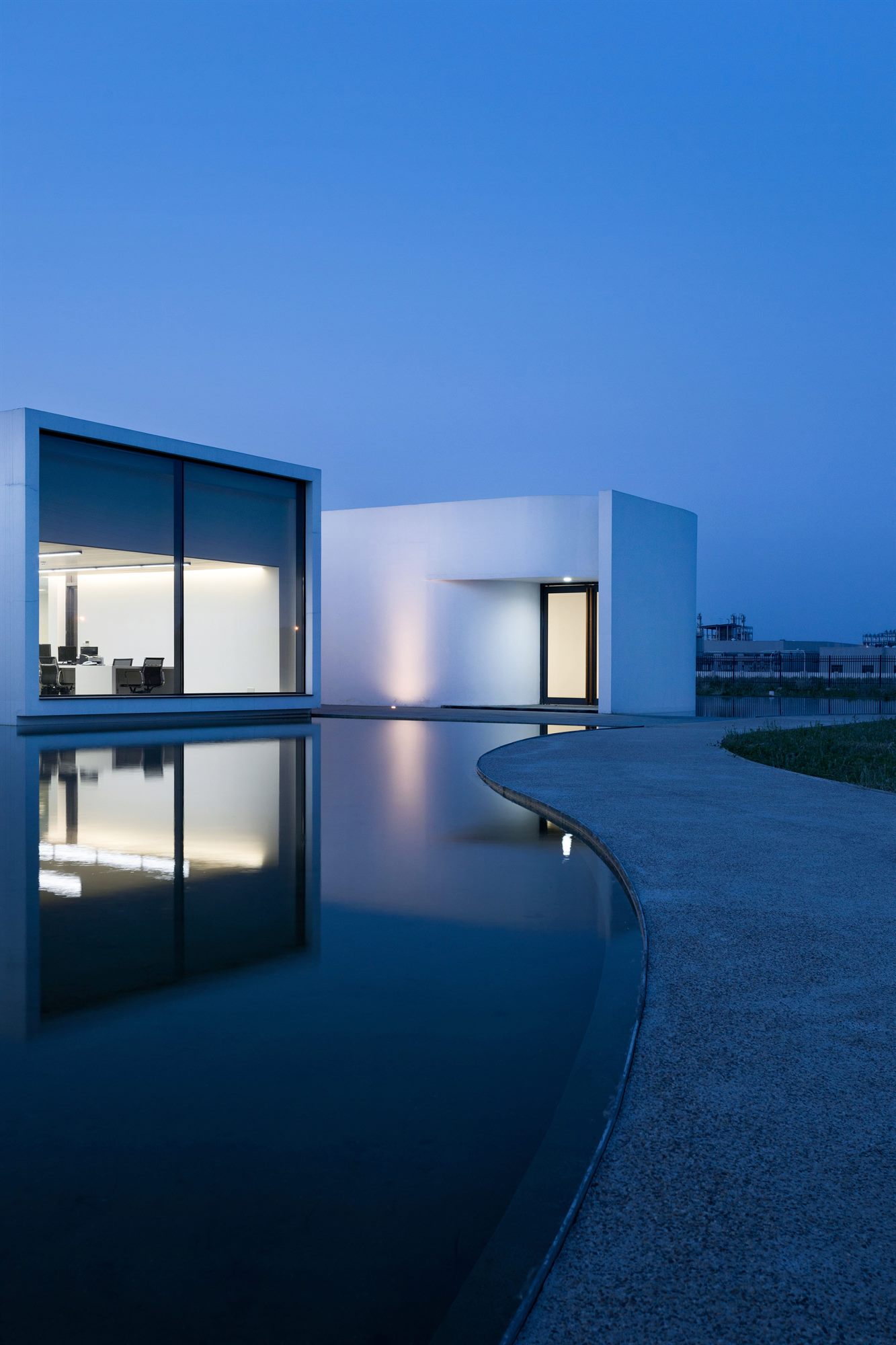 Salt laboratory at dusk, white volumes and lit windows reflected in water
