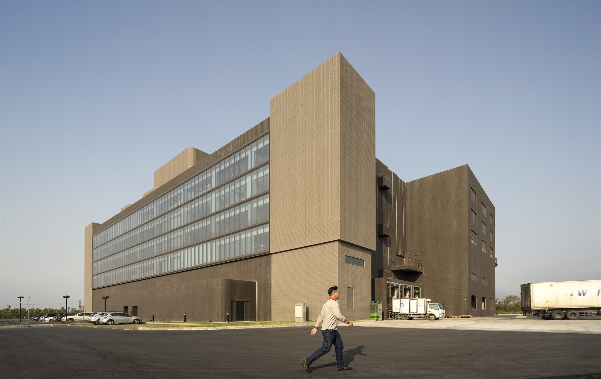 Corner of the T-HAM factory: glazed office floors set into the production building, clad in locally made grey textured tiles