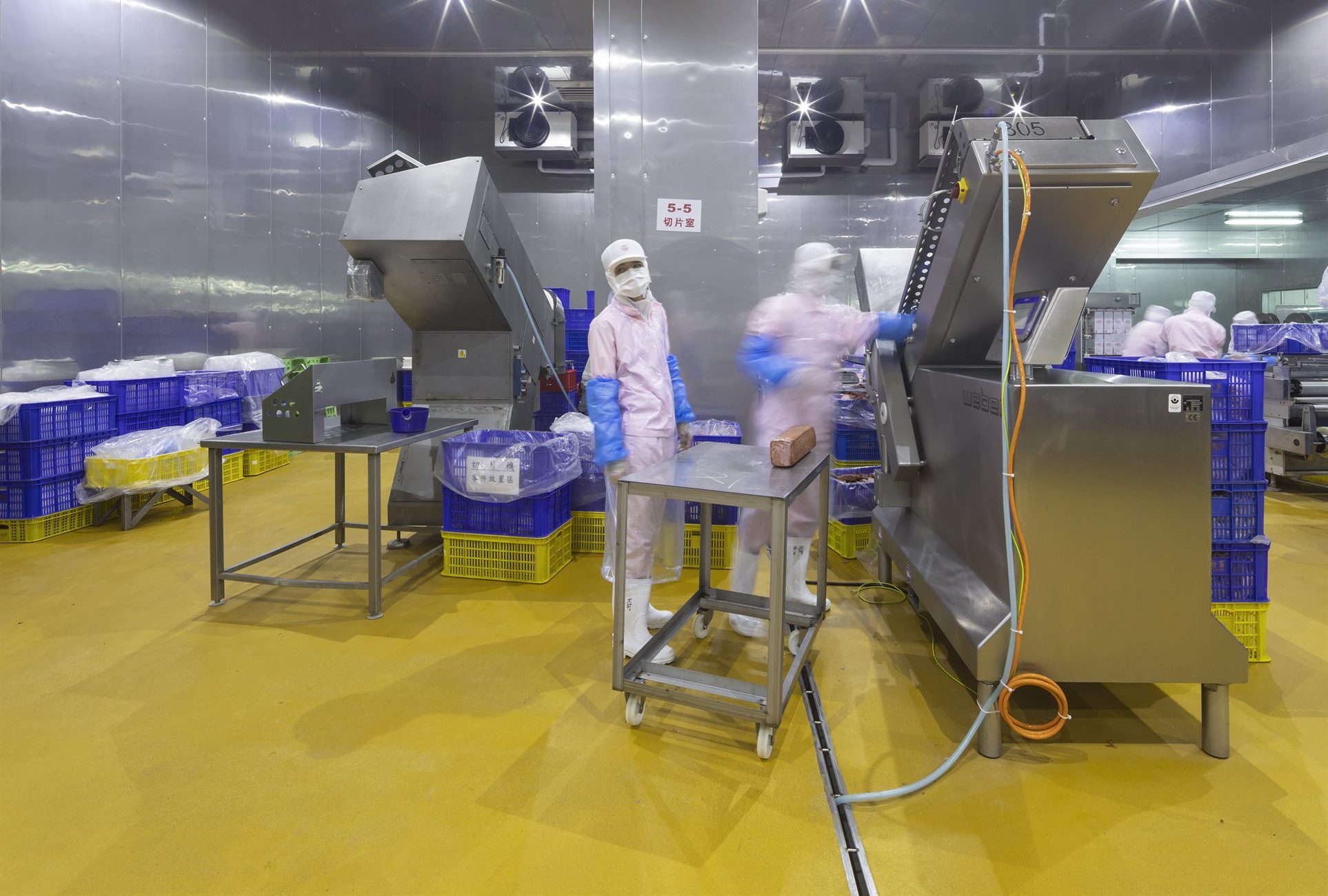 Workers in hygiene suits operating processing machinery on the T-HAM production floor