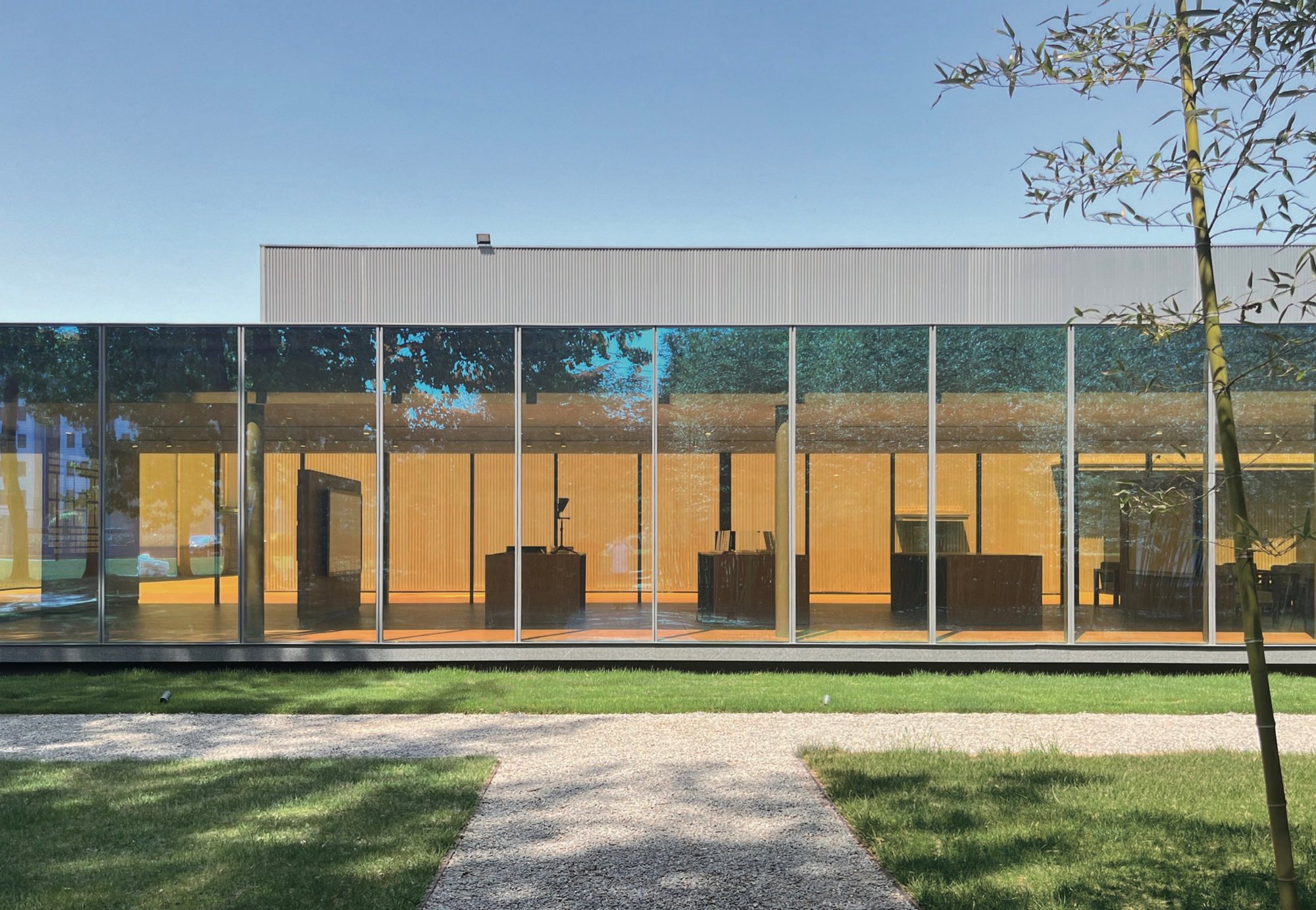 Yellow-toned dichroic glass showroom behind a lawn, Qingdao